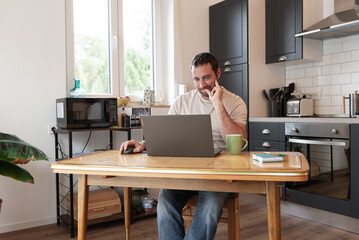 Concentrated man e-learning with his laptop from his kitchen.