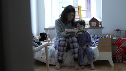 Candid mother telling story to child in bedroom. Authentic real life parenting scene of mom holding...