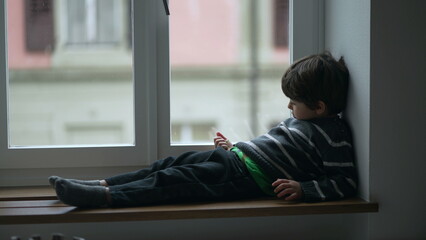 Lazy child sliding down by apartment window, candid bored kid at home with nothing to do, kid...