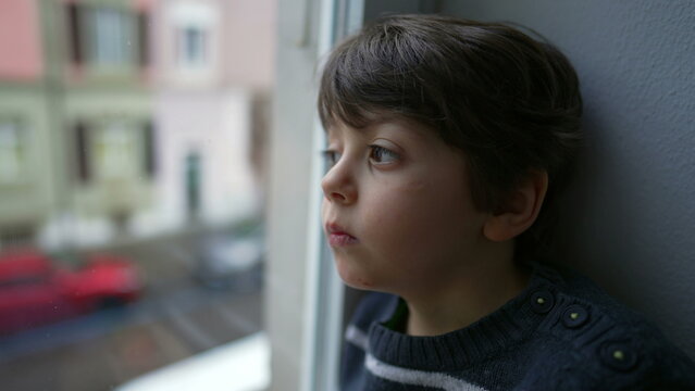 Sad and Bored Little Boy Sitting by Window, Staring in Melancholy, Wanting to Go Out but Stuck at Home