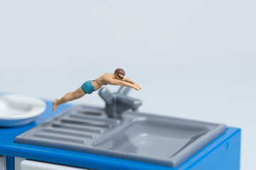 A swimmer makes a head dive into a kitchen sink , miniature figures scene,