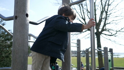 Active small boy sliding down metal bar at playground during fall season, child wearing jacket and...