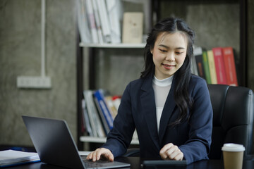 Asian businesswoman using a laptop computer sitting at desk in office.