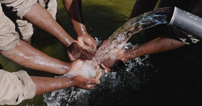 Slow motion. Close-up. Cropped view. Small group of Black peoples hands catching clean running water out a pipe