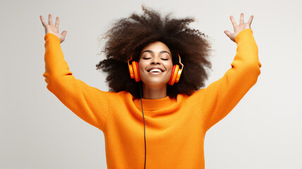Happy young Afro American woman carried away with music dances carefree with arms raised keeps eyes closed wears stereo headphones on ears dressed in orange jumper isolated over white background - obrazy, fototapety, plakaty