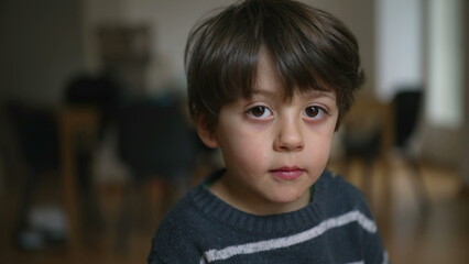 Portrait of a 4 year old boy close-up face looking at camera with neutral expression indoors
