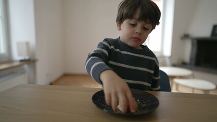 Fototapeta premium Small boy eating piece of bread, close-up 4 year old child snacking carb food sitting at table indoors