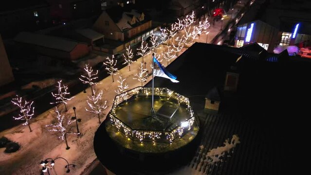 Estonian flag on Tower in the the city of Voru, Estonia. Beautiful winter landscape with Estonia flag waving in the wind. Christmas lights flickering in the background. Christmas holiday 