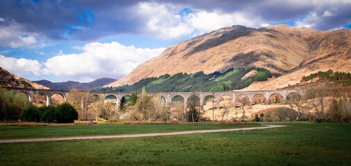 Glenfinnan Viaduct, train bridge, Glenfinnan, Scotland. Famous viaduct in Scottish Highlands, near Fort William, surrounded by hills, blue sky and clouds on a sunny day. - obrazy, fototapety, plakaty