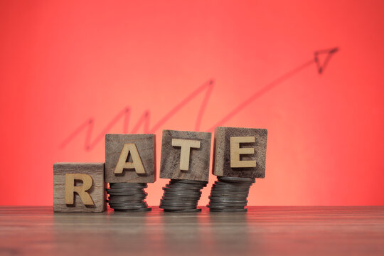Wooden cube with the word RATE on the stacked coins. A graph pointing upward with a blur effect at the back.