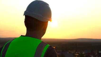 Silhouette of a man in a work helmet against the background of the setting sun.