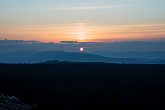 Morning sun rises above the horizon, silhouettes of mountains, dark views of mountainous terrain, early morning, yellow disk of the sun.