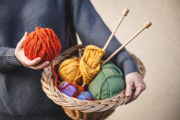 Woman holding ball of wool for knitting or crochet. Colorful yarn in wicker basket - obrazy, fototapety, plakaty