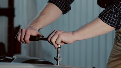 An auto mechanic is working on a car engine in a car workshop. Close-up ratchet wrench