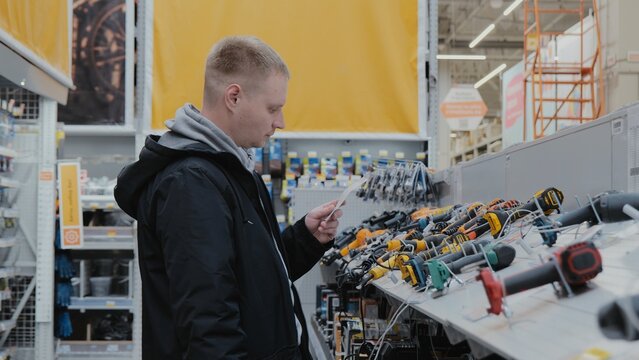 Buying a screwdriver at a hardware store. A man in a hardware store buys a power tool. Cordless power tools. Construction equipment supermarket