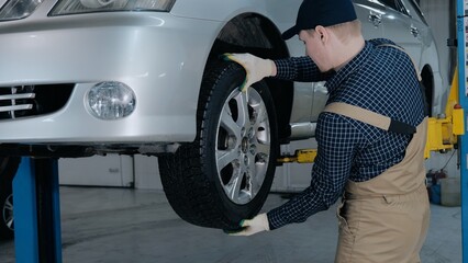 Inspection of the chassis of the car. A young mechanic in uniform works in a car service with a...