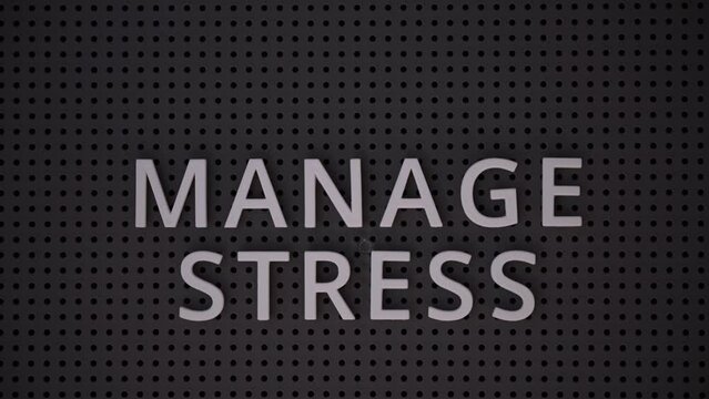 Words Manage Stress spelled out with white letters on a gray pegboard