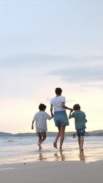 A mother and her 5 and 7-year-old children walk along the beach near the water at sunset on a paradisiacal island. Enjoying quality family time, motherhood, and childhood memories. Summer beach sunset