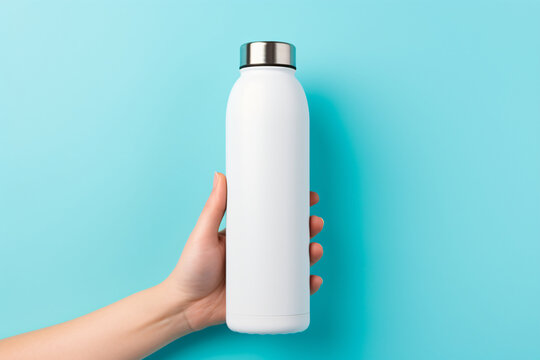 A hand holding a reusable steel stainless eco thermo water bottle on a blue background. This image can be used for a variety of purposes, such as product photography, marketing, and advertising.