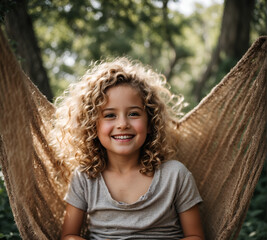 A little blond girl with curly hair, smiling sitted in a hammock.