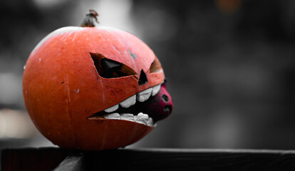 Halloween spooky pumpkin decoration. Selective color image of orange pumpkin with evil face. Dark blurry background with copy space.