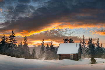 A winter landscape featuring a wooden cabin and snow-covered fir trees on a mountain clearing....