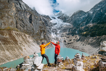 Trekkers couple dressed bright waterproof jackets giving High Five enjoying glacier falling in high...