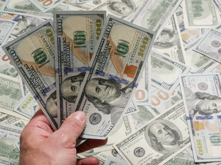 Three 100 dollar bills in a man's hand, close-up.