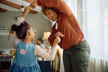 Happy black mature woman and her granddaughter dancing at home.