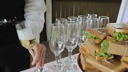 Catering with sandwiches. A young woman pours champagne into glasses. A woman pours champagne into a glass, close-up.
