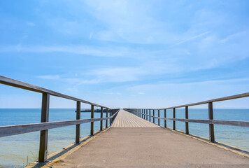 Wooden walkway to the sea and blue sky with white clouds
