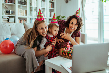 Happy young lesbian family sharing the birthday of their child on a laptop video call at home