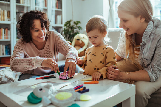 Happy young lesbian couple drawing and having fun with their daughter in the living room at home