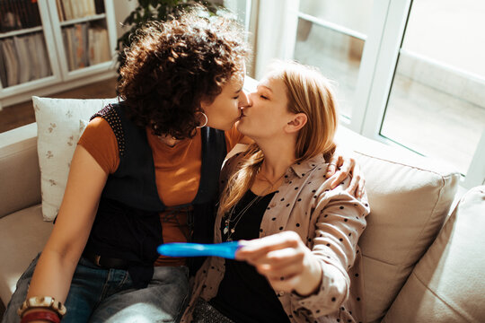 Young lesbian couple sharing a kiss after a positive pregnancy test at home