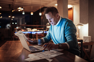 Middle aged man going over financials with a laptop at home during night