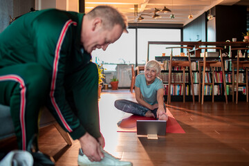 Mature woman doing yoga while her husband prepares to leave out and jog in the neighborhood