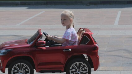 A little girl rides a car. The girl is driving a children's car.