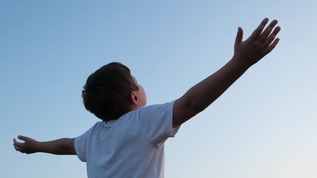 a cute boy is raising his hands to the sky and spinning and looking at the sky.
