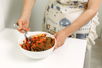 A woman stirs the ingredients for making adjika in a plate with a spoon.