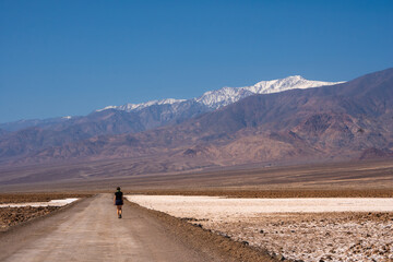 Fototapeta premium Woman walking in Badwater basin and its salt flats in bright spring daylight, Death Valley, California, USA. Telescope peak in the distance.