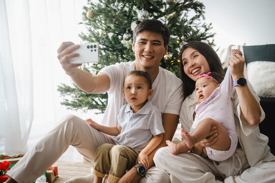 Asian family taking a selfie photo by using a smartphone while celebrating Christmas in the living room