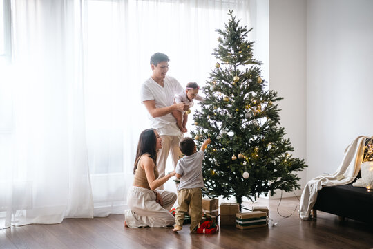 Happy Asian family decorating Christmas tree together in the living room at home. They are putting on various baubles and ornaments and enjoying their holiday