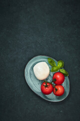 Fresh cherry tomatoes, basil, mozzarella cheese on black slate stone table. Healthy Italian traditional salad ingredients. The concept of organic Mediterranean cuisine, apartment, close-up.