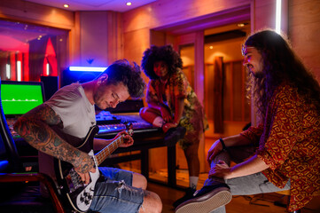 Music producer trying a bass riff while bassist and singer are watching. - obrazy, fototapety, plakaty