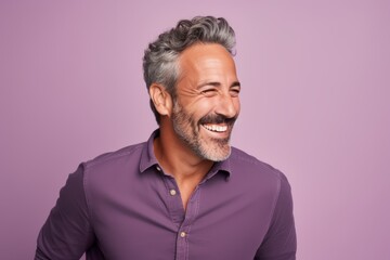 Handsome mature man smiling and looking at camera against purple background