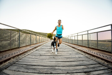 Frontal photo of an adult runner with an amputated arm running on an outdoor bridge with a dog...