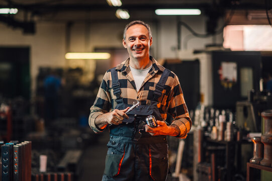 Portrait of a happy mechanic holding a caliper and a metal part in a workshop.