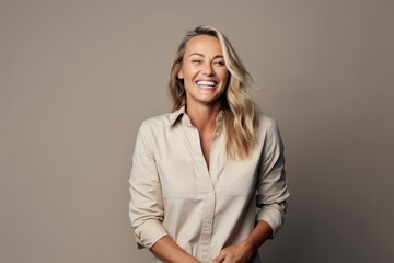 Happy young woman laughing and looking at camera while standing against grey background