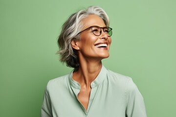 Happy mature woman in eyeglasses smiling and looking up against green background