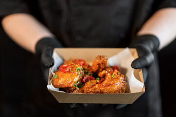 The cook holds in his hands a box with grilled spicy chicken